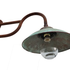 May include: A rusty metal wall sconce with a green copper shade and a clear glass globe. The sconce has a curved arm and a rectangular base.