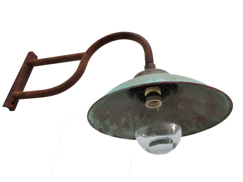 May include: A rusty metal wall sconce with a green copper shade and a clear glass globe. The sconce has a curved arm and a rectangular base.