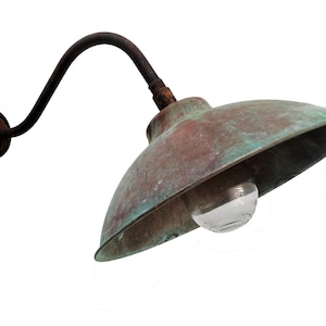 May include: A vintage copper outdoor wall light fixture with a curved arm and a green patina. The light has a clear glass globe and is mounted on a wall.