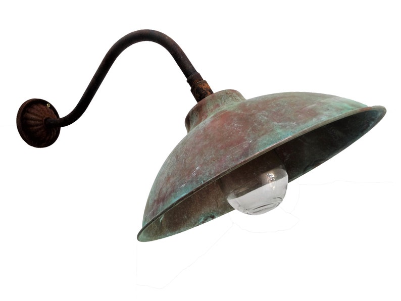 May include: A vintage copper outdoor wall light fixture with a curved arm and a green patina. The light has a clear glass globe and is mounted on a wall.