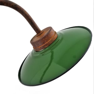 May include: A green metal lampshade with a brown wooden base and a curved metal arm. The lampshade is attached to the arm with a metal screw.