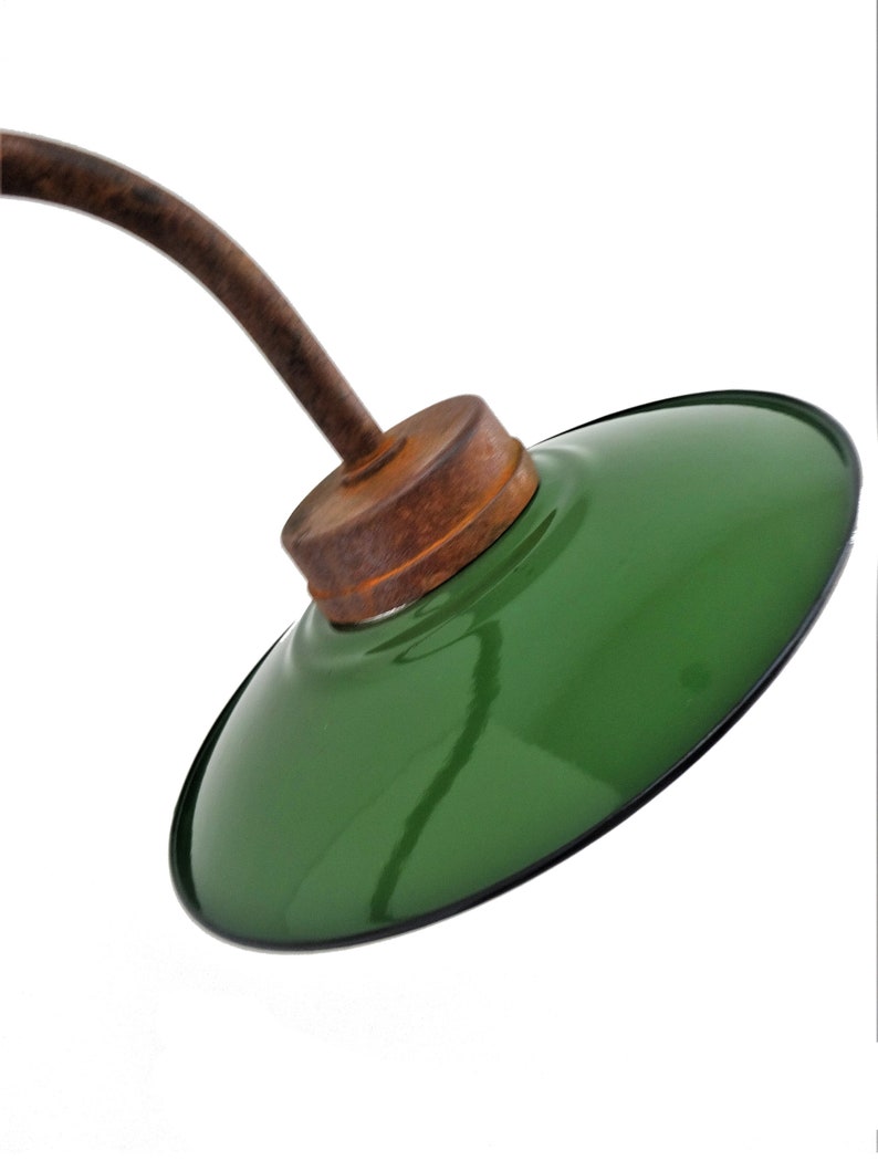 May include: A green metal lampshade with a brown wooden base and a curved metal arm. The lampshade is attached to the arm with a metal screw.