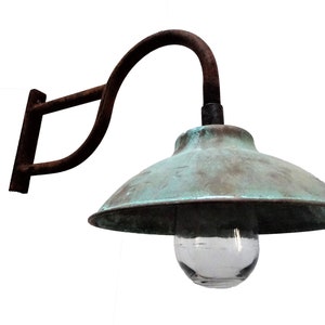 May include: A vintage, rusty metal wall sconce with a copper-colored shade and a clear glass globe. The sconce has a curved arm and a simple, rectangular wall mount.