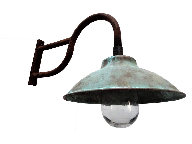 May include: A vintage, rusty metal wall sconce with a copper-colored shade and a clear glass globe. The sconce has a curved arm and a simple, rectangular wall mount.