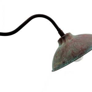 May include: A vintage-style wall-mounted light fixture with a curved arm and a copper-colored shade. The shade has a weathered patina and a light bulb is visible inside.
