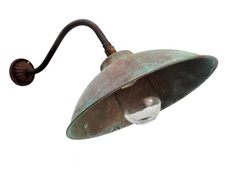May include: A vintage copper outdoor wall light fixture with a curved arm and a domed shade. The light is weathered and has a green patina.