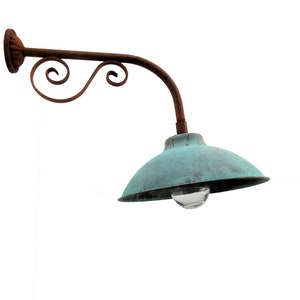 May include: A rusty metal wall-mounted lamp with a curved arm and a green metal shade. The lamp has a decorative scroll design on the arm.