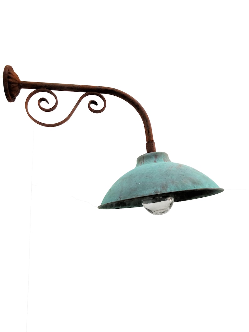 May include: A rusty metal wall-mounted lamp with a curved arm and a green metal shade. The lamp has a decorative scroll design on the arm.