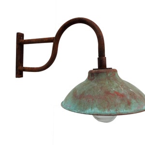 May include: A rusty metal wall-mounted light fixture with a copper-colored shade. The shade has a green patina and a clear glass light bulb.