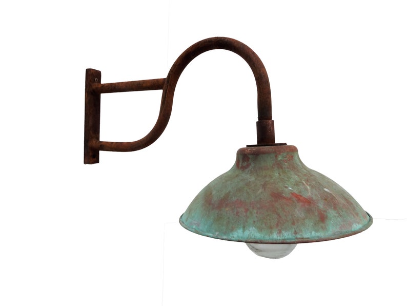 May include: A rusty metal wall-mounted light fixture with a copper-colored shade. The shade has a green patina and a clear glass light bulb.