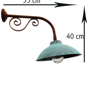 May include: A rustic, green metal outdoor wall light with a decorative scrollwork arm. The light is 55 cm wide and 40 cm tall.