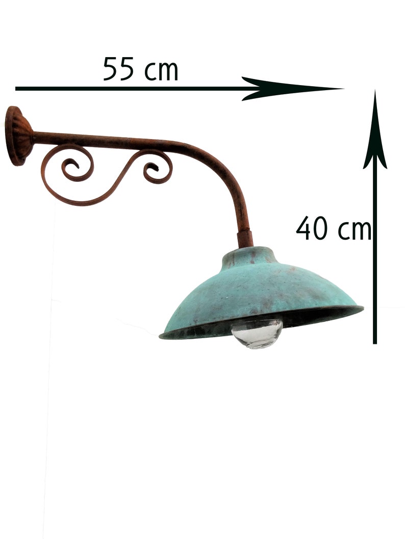 May include: A rustic, green metal outdoor wall light with a decorative scrollwork arm. The light is 55 cm wide and 40 cm tall.