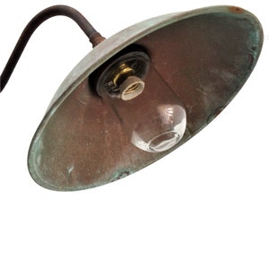 May include: A vintage copper outdoor light fixture with a clear glass bulb. The light fixture has a curved arm and a rounded shade.