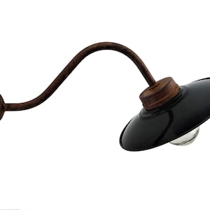 May include: A black metal wall sconce with a curved arm and a black enamel shade. The sconce has a rustic, industrial look and is perfect for adding a touch of vintage style to any room.