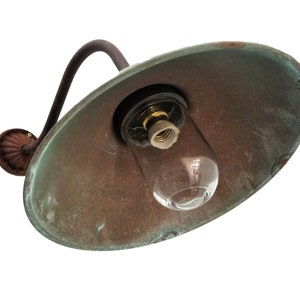 May include: A vintage copper-colored outdoor wall light fixture with a clear glass globe and a curved arm. The light fixture has a weathered patina and is designed for a single bulb.