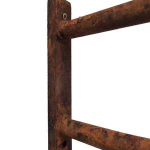May include: A rusty metal wall-mounted towel rack with two bars. The rack is attached to the wall with screws. The metal is heavily rusted and has a brown and orange color.