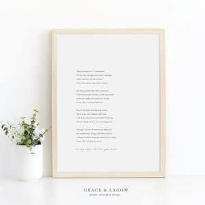 May include: A framed print with a poem about remembering places and people in life. The poem reads, "There are places I'll remember all my life, though some have changed some have stayed, and some have gone, but some have grown, and some remain... In my life, I'll love you more." The print is on a white background and has a light wood frame. The print is sitting on a white surface with a small potted plant in front of it.