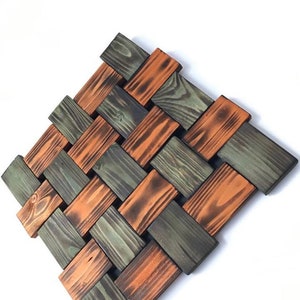 May include: A woven wall art piece made of wood with a geometric pattern. The wood is stained in shades of green and orange.