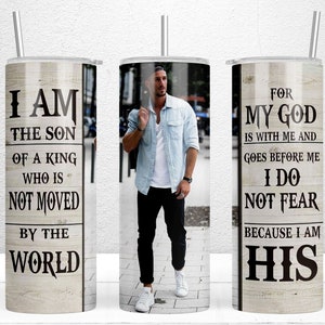 May include: A stainless steel tumbler with a straw, featuring a man in a light blue shirt and black pants. The tumbler has text that reads "I AM THE SON OF A KING WHO IS NOT MOVED BY THE WORLD" and "FOR MY GOD IS WITH ME AND GOES BEFORE ME I DO NOT FEAR BECAUSE I AM HIS."