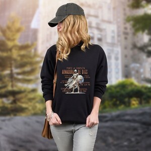 Pode incluir: Camisola de moletom preta com um gr&aacute;fico de um cavaleiro de armadura e o texto "Ponte la completa armadura de Dios" em espanhol. O texto est&aacute; em dourado e o cavaleiro est&aacute; em branco.