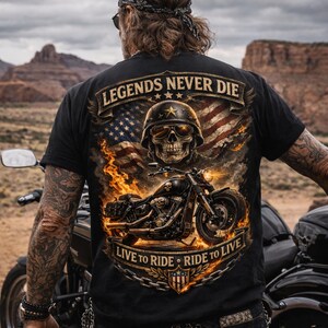 May include: Black t-shirt featuring a motorcycle graphic with a skull wearing a helmet and sunglasses, set against an American flag and flames. The text "LEGENDS NEVER DIE" and "LIVE TO RIDE - RIDE TO LIVE" are displayed on the shirt.