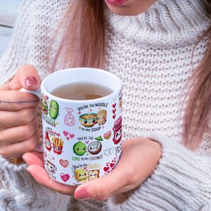 May include: A white ceramic mug with a variety of food-themed illustrations and text. The mug features images of a pickle burger, ketchup, fries, and other food items. Text includes "You're the Noodle to my Soup" and "Lime to my Coconut."