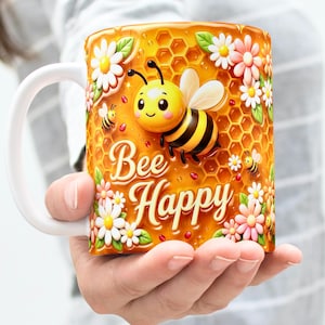 Peut inclure: Mug en céramique blanche avec un motif enveloppant représentant une abeille de dessin animé, un motif en nid d'abeille et des accents floraux. La tasse porte les mots "Bee Happy". La tasse est tenue dans les mains d'une personne.