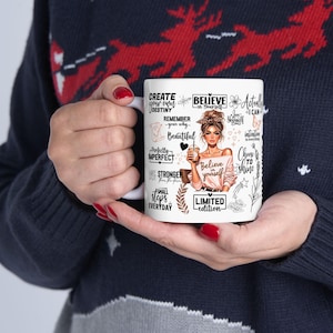 K&ouml;nnte beinhalten: Wei&szlig;er Keramikbecher mit inspirierenden Zitaten und Illustrationen, darunter eine Frau, die eine Kaffeetasse h&auml;lt. Der Becher enth&auml;lt S&auml;tze wie "Glaube an dich selbst" und "Erschaffe dein eigenes Schicksal". Limitierte Auflage.