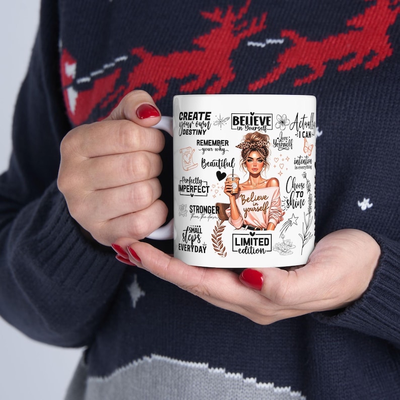 K&ouml;nnte beinhalten: Wei&szlig;er Keramikbecher mit inspirierenden Zitaten und Illustrationen, darunter eine Frau, die eine Kaffeetasse h&auml;lt. Der Becher enth&auml;lt S&auml;tze wie "Glaube an dich selbst" und "Erschaffe dein eigenes Schicksal". Limitierte Auflage.