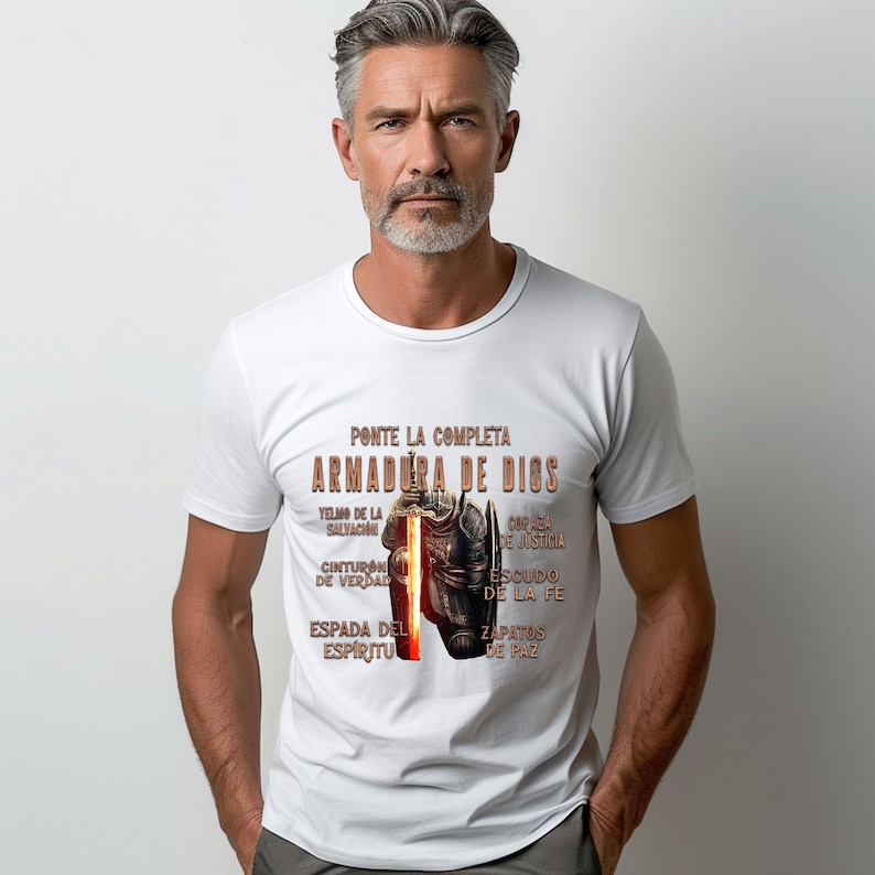 May include: White t-shirt with a graphic of a knight in armor and the text "PONTE LA COMPLETA ARMADURA DE DIOS" in Spanish. The text is surrounded by a list of armor pieces, including "YELMO DE LA SALVACION", "CINTURON DE VERDAD", "ESPADA DEL ESPIRITU", "COPA DE JUSTICIA", "ESCUDO DE LA FE", and "ZAPATOS DE PAZ".