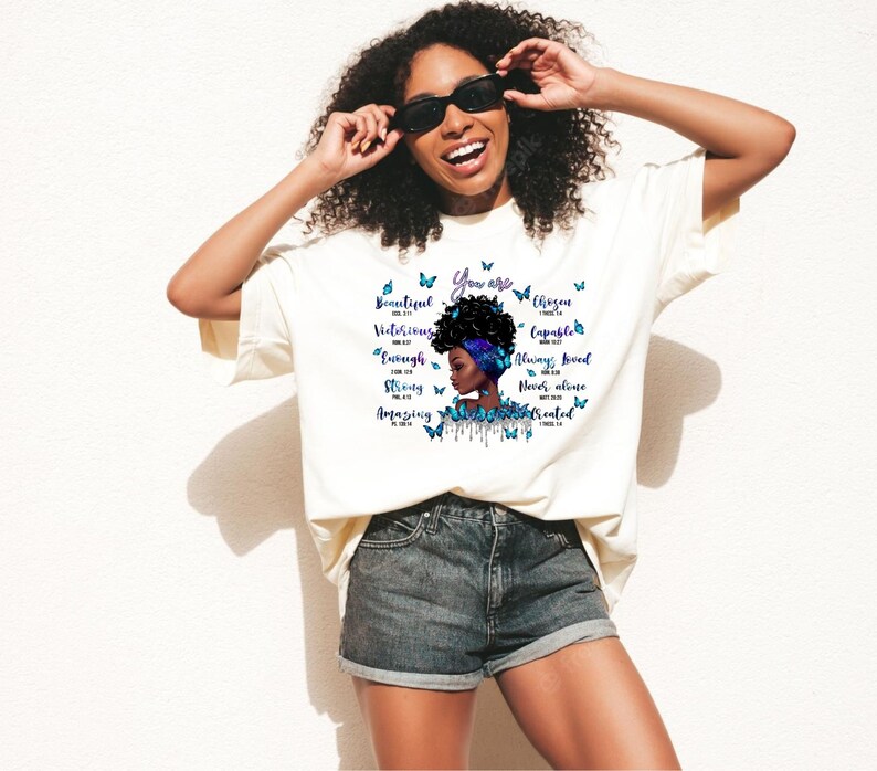 May include: A white t-shirt with a graphic design of a black woman with blue butterflies and inspirational text. The text reads "You are Beautiful, Victorious, Capable, Enough, Strong, Amazing, Always Loved, Never Alone,  Treated".