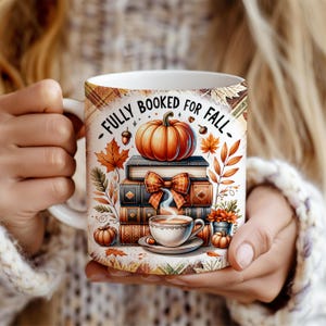 Könnte beinhalten: Weiße Keramik-Tasse mit herbstlichem Design. Die Tasse zeigt einen Stapel Bücher, einen Kürbis, Herbstblätter und eine Tasse Kaffee. Der Text auf der Tasse lautet "FULLY BOOKED FOR FALL".