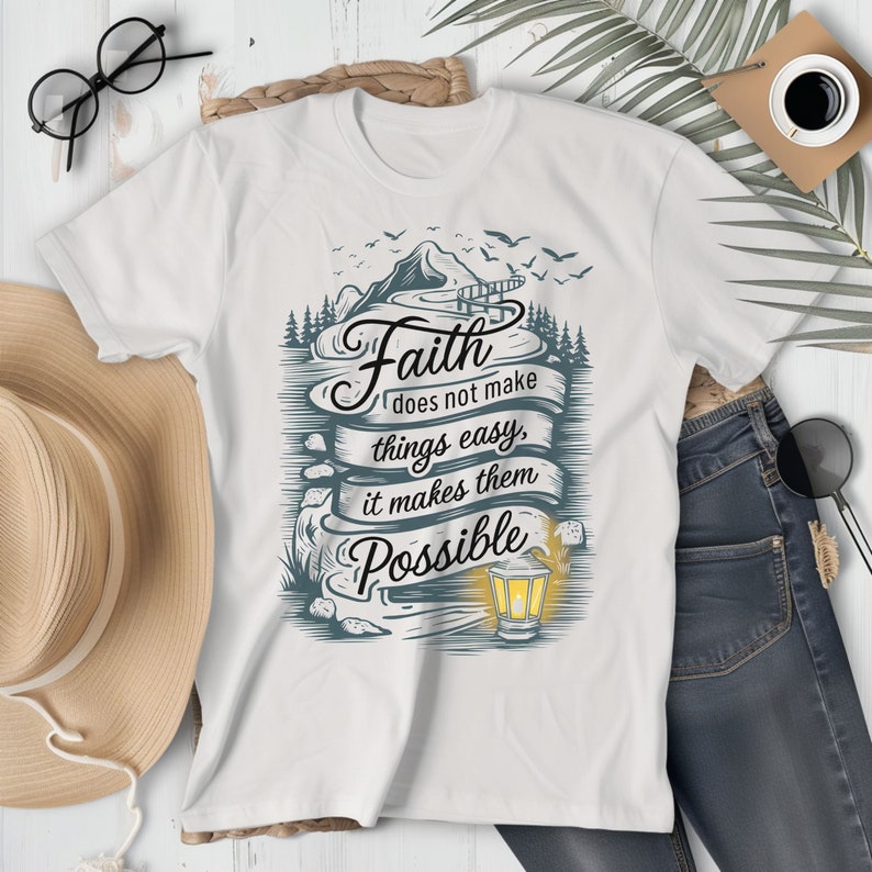 May include: White t-shirt with a graphic design of a mountain landscape, a bridge, and a lantern. The text "Faith does not make things easy, it makes them Possible" is written on a banner.