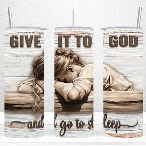 May include: A stainless steel tumbler with a straw, featuring a design of a woman resting her head on a surface. The text "GIVE IT TO GOD and I go to sleep" is displayed in brown lettering against a white and wood-grain background.