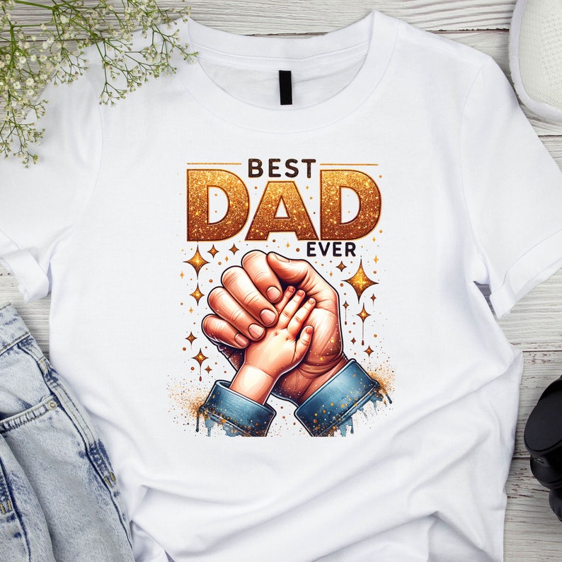 May include: White t-shirt with a gold glitter graphic that says "Best Dad Ever". The graphic also features a father and child holding hands.