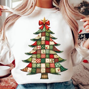 Può includere: Felpa bianca con un design ad albero di Natale. L'albero è composto da quadrati patchwork rossi, verdi e beige, sormontato da un fiocco rosso e una stella dorata. Il design ha un tema festivo e natalizio.