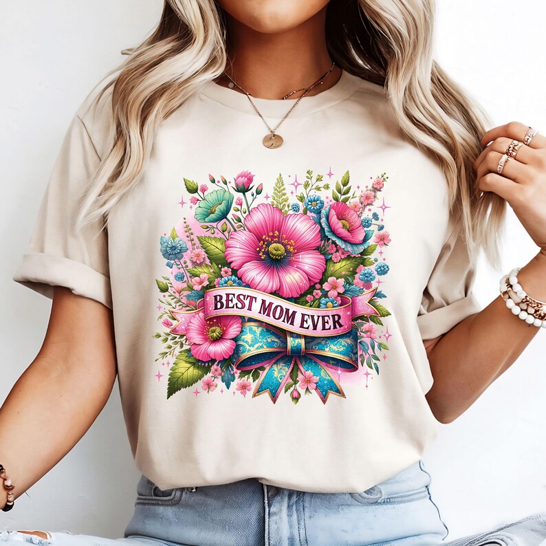 Op de afbeelding: Een beige T-shirt met een bloemenontwerp en de tekst "Best Mom Ever" op een blauw lint met strik.