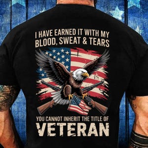 Könnte beinhalten: Schwarzes T-Shirt mit einem abgenutzten amerikanischen Flaggen-Design und einem Adler. Der Text lautet "Ich habe es mir mit meinem Blut, Schweiß und Tränen verdient. Den Titel VETERAN kann man nicht erben."