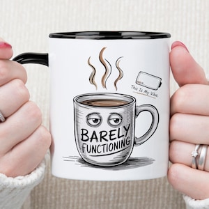 May include: White ceramic coffee mug with a black rim and handle. The mug features a cartoon illustration of a coffee cup with the words "Barely Functioning" and the phrase "This Is My Vibe."