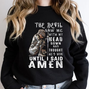 May include: Black sweatshirt with a graphic of a woman in armor kneeling with a sword. The text reads "The Devil Saw Me With My Head Down And Thought He'd Won Until I Said Amen."