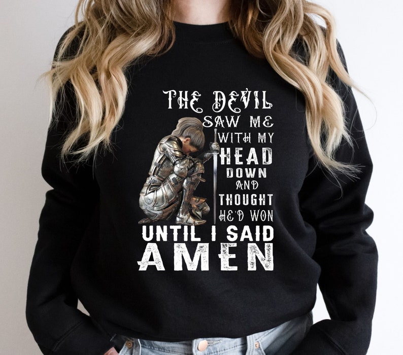 May include: Black sweatshirt with a graphic of a woman in armor kneeling with a sword. The text reads "The Devil Saw Me With My Head Down And Thought He'd Won Until I Said Amen."