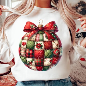 Könnte beinhalten: Weißes Sweatshirt mit einem großen, farbenfrohen Weihnachtsbaumschmuck-Design. Der Schmuck ist ein Patchwork aus roten, grünen und weißen Mustern, gekrönt von einer roten Schleife und goldfarbener Hardware. Das Design umfasst Herzen, Poinsettien und Karos.