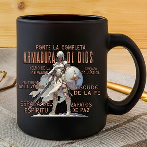 Pode incluir: Caneca de cer&acirc;mica preta com um design branco e dourado que apresenta uma mulher com armadura e o texto "PONTE LA COMPLETA ARMADURA DE DIOS" com as palavras "YELMO DE LA SALVACI&Oacute;N", "CINTURON DE LA VERDAD", "ESPADA DEL ESP&Iacute;RITU", "CORAZA DE JUSTICIA", "ESCUDO DE LA FE" e "ZAPATOS DE PAZ" ao redor da imagem.