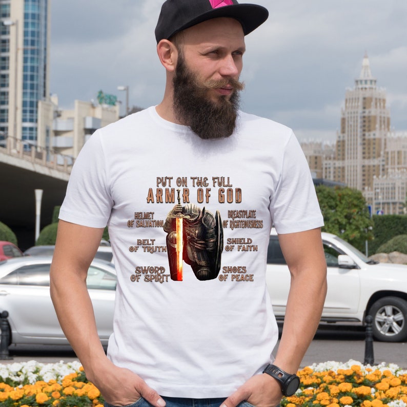 May include: White t-shirt with a graphic of a knight in armor holding a sword. The text "Put on the full Armor of God" is printed on the shirt, along with the words "Helmet of Salvation", "Breastplate of Righteousness", "Belt of Truth", "Shield of Faith", "Sword of Spirit", and "Shoes of Peace".