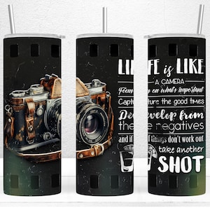 May include: A black and white tumbler with a vintage camera and film strip design. The tumbler has the text "Life is like a camera. Focus on what's important. Capture the good times. Develop from the negatives. And if things don't work out, take another shot."