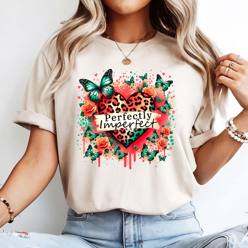 May include: A beige t-shirt with a graphic print of a leopard print heart with butterflies and flowers. The text "Perfectly Imperfect" is printed on the heart.