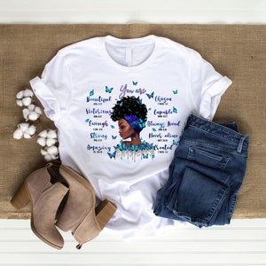 May include: White t-shirt with a black and blue illustration of a woman's face with butterflies and the text "You are Beautiful, Victorious, Enough, Strong, Amazing, Chosen, Capable, Always Loved, Never Alone, Created".