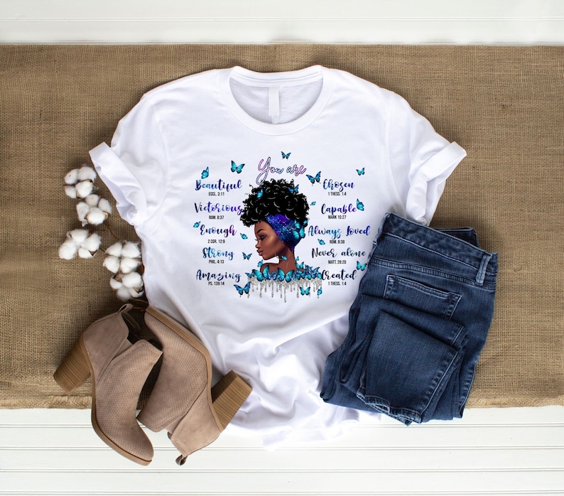 May include: White t-shirt with a black and blue illustration of a woman's face with butterflies and the text "You are Beautiful, Victorious, Enough, Strong, Amazing, Chosen, Capable, Always Loved, Never Alone, Created".