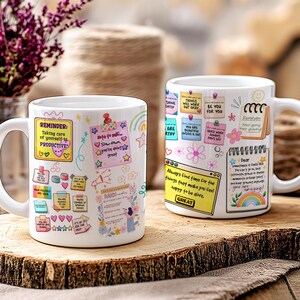 May include: Two white ceramic mugs with colorful motivational notes and illustrations. One mug features the text "Reminder: Taking care of yourself is PRODUCTIVE." The other mug has the text "Always find time for the things that make you feel happy to be alive."