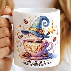 Könnte beinhalten: Weiße Keramik-Tasse mit einem fantasievollen Design. Ein blauer Zaubererhut liegt über einer Kaffeetasse, mit einem Sternenstab. Die Tasse ist mit Kaffeebohnen und Sternen verziert, und der Text lautet "Mornings: Powered by Magic Bean Juice."